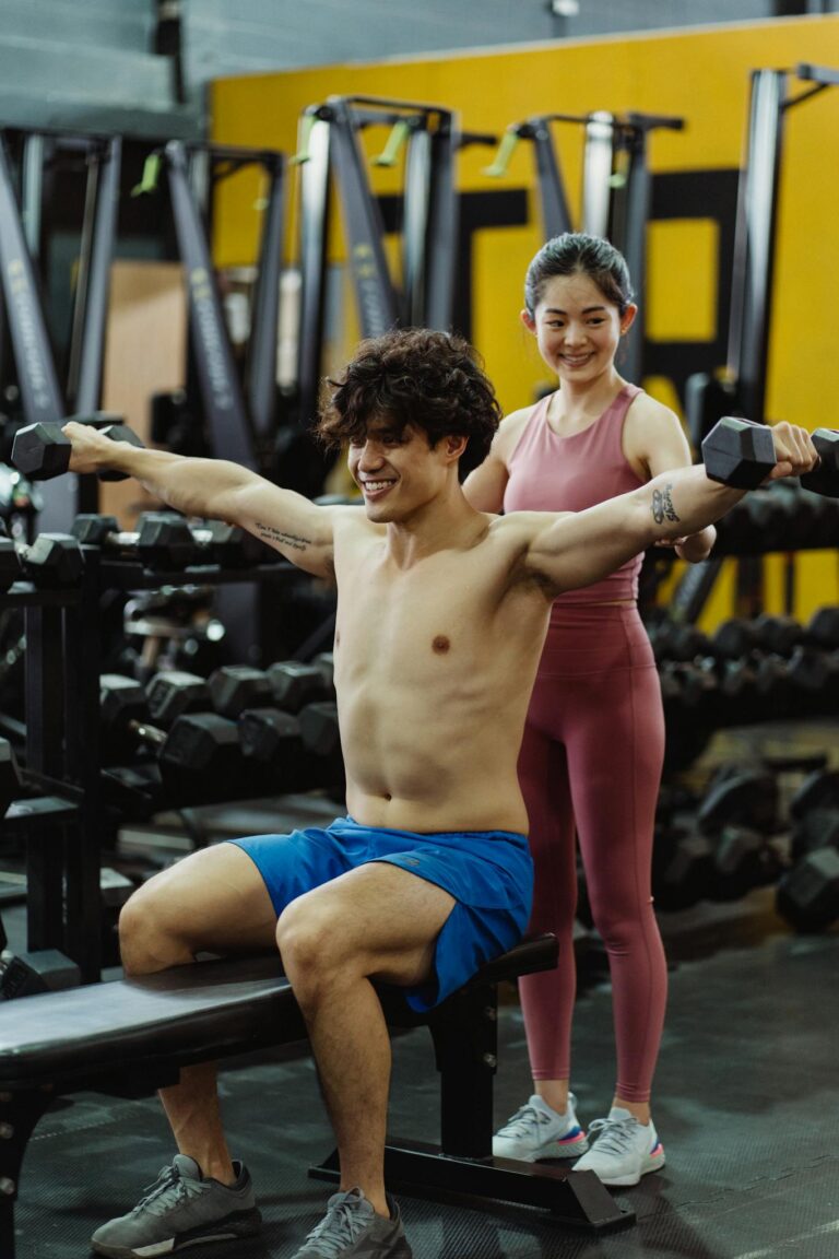 A personal trainer assists a man lifting weights in a gym setting, emphasizing fitness coaching.